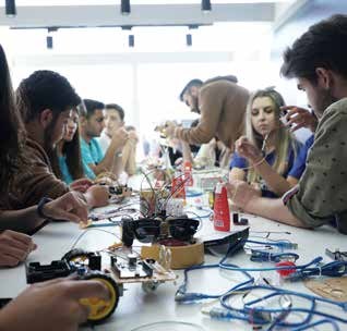 Bir masa etrafında elektronik devreler ve robotik malzemelerle çalışan katılımcılar