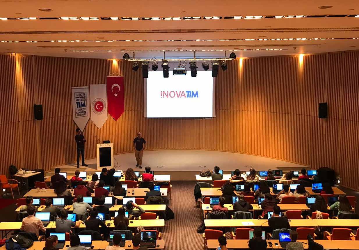 İnovaTİM logosunun yansıtıldığı salonda bilgisayarlarıyla eğitime katılan kişiler